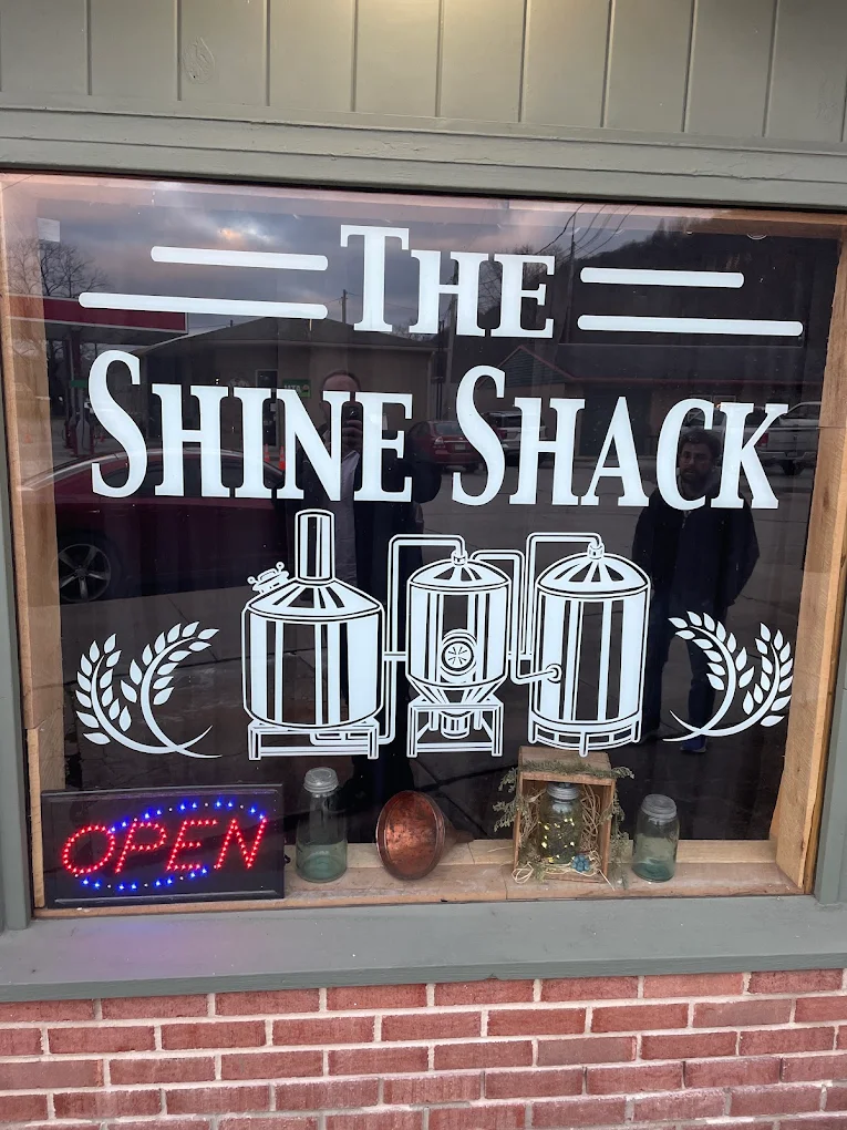 The Shine Shack storefront window with hand-painted signage and copper stills in Confluence, PA